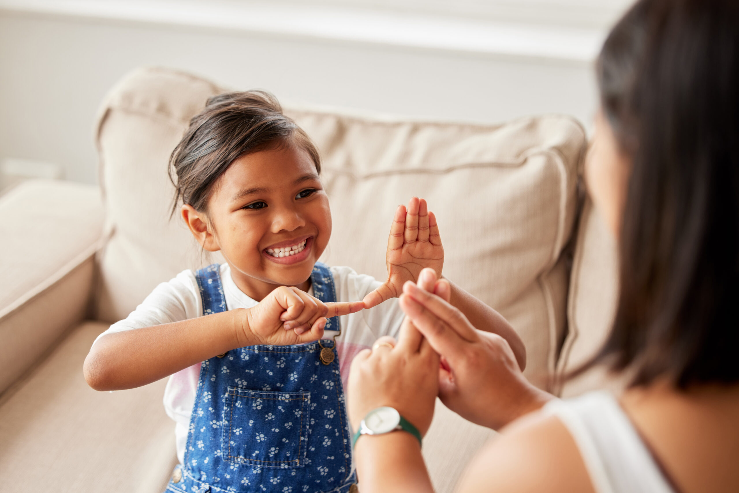Cute child using sign language to communicate and talk with her mother at home.